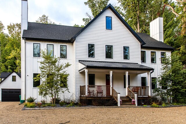 view of front of home with a porch, a standing seam roof, a chimney, a garage, and an outdoor structure