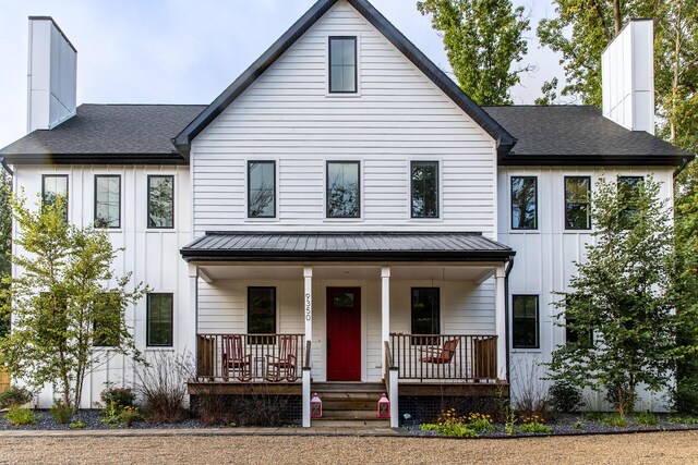modern inspired farmhouse featuring board and batten siding, covered porch, a standing seam roof, metal roof, and a chimney