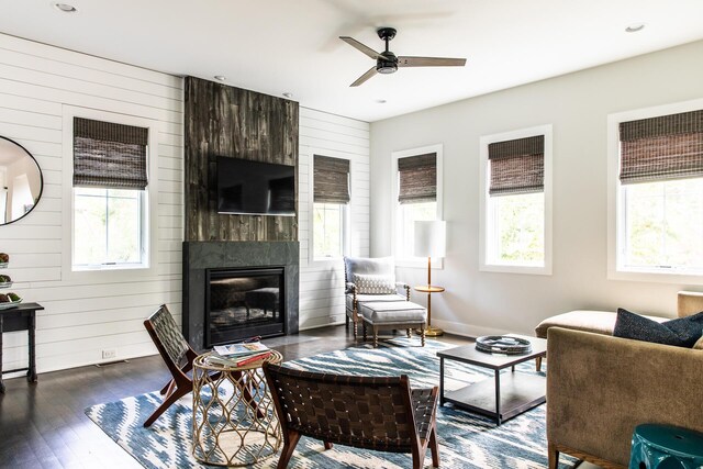 living area featuring a healthy amount of sunlight, a large fireplace, wood walls, and dark wood-style flooring