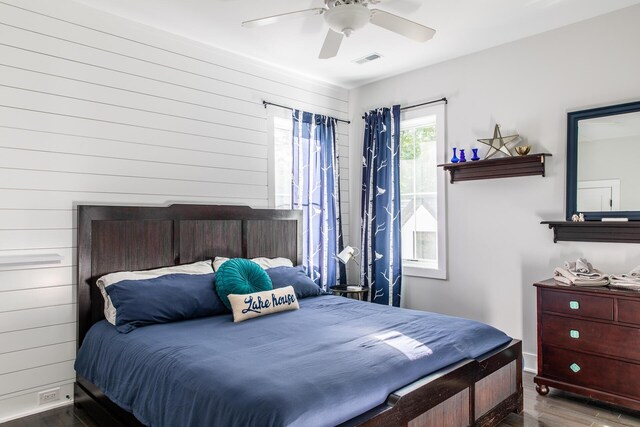 bedroom with visible vents, wood finished floors, baseboards, ceiling fan, and wooden walls