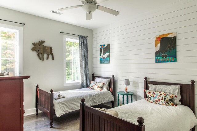 bedroom featuring visible vents, wood walls, wood finished floors, baseboards, and a ceiling fan