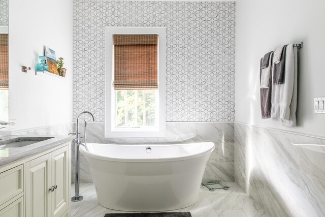 bathroom featuring a freestanding bath, vanity, a wainscoted wall, wallpapered walls, and tile walls