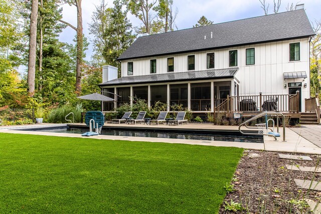 back of property featuring a shingled roof, a sunroom, an outdoor pool, a lawn, and a patio