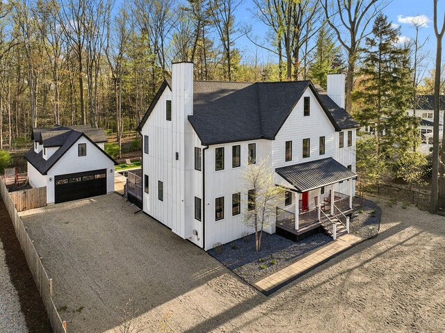 modern farmhouse with a shingled roof, a detached garage, an outdoor structure, and a chimney
