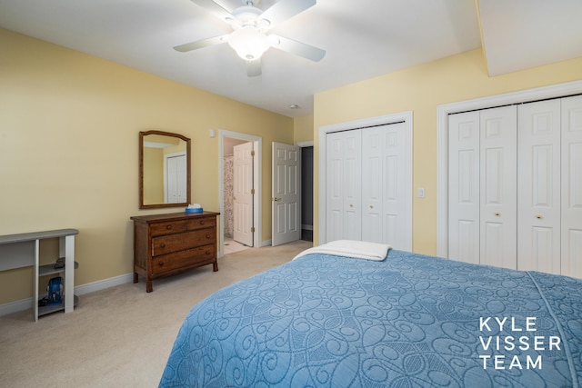 bedroom with multiple closets, baseboards, ceiling fan, light colored carpet, and ensuite bath