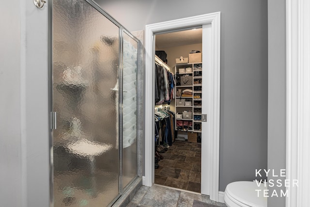 full bathroom with a walk in closet, a stall shower, toilet, and stone finish flooring