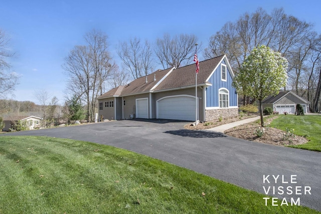 view of side of property featuring board and batten siding, a lawn, aphalt driveway, an attached garage, and stone siding