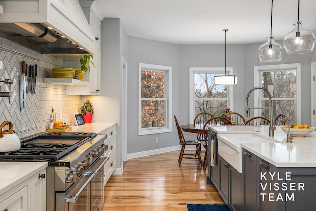 kitchen featuring stainless steel stove, wall chimney exhaust hood, tasteful backsplash, a sink, and light wood finished floors