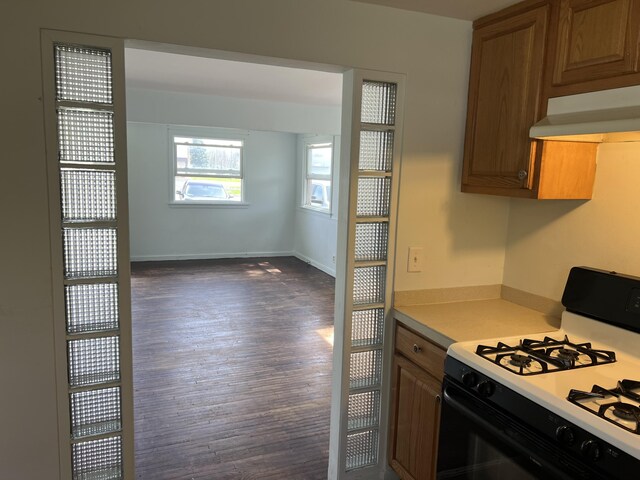 kitchen with gas range, brown cabinets, dark wood finished floors, light countertops, and under cabinet range hood
