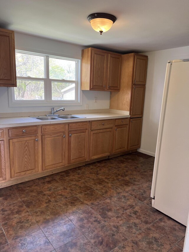 kitchen with a sink, light countertops, freestanding refrigerator, and brown cabinets