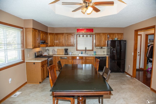 kitchen with brown cabinets, a sink, plenty of natural light, under cabinet range hood, and black appliances