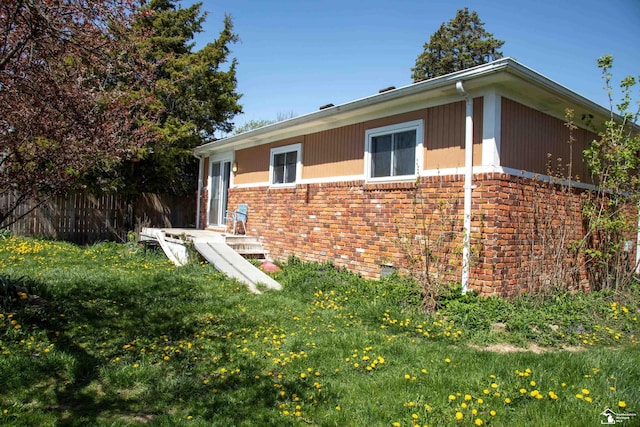 view of property exterior with brick siding, a lawn, and fence