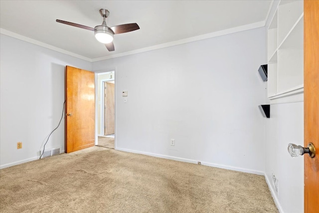 carpeted spare room featuring visible vents, crown molding, baseboards, and ceiling fan