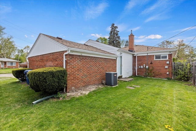 view of side of property featuring fence, central AC unit, a lawn, and brick siding