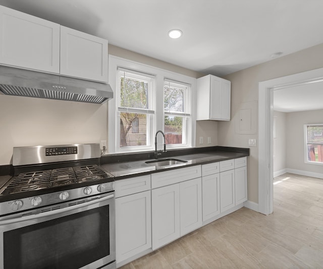 kitchen featuring dark countertops, stainless steel gas range, white cabinetry, under cabinet range hood, and a sink
