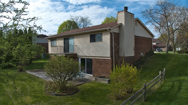 rear view of house with a lawn, fence, a chimney, and brick siding