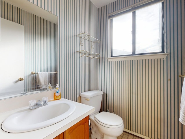 half bathroom with vanity, toilet, and wallpapered walls