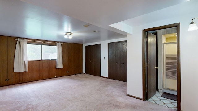 unfurnished bedroom featuring light colored carpet, multiple closets, baseboards, and visible vents