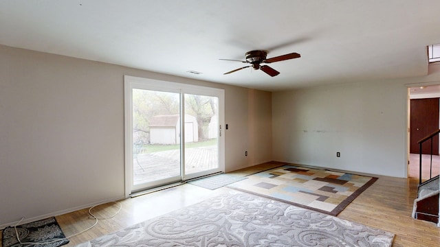 empty room featuring a ceiling fan, visible vents, baseboards, light wood finished floors, and stairs
