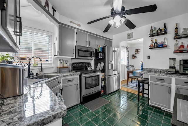 kitchen featuring a ceiling fan, a sink, gray cabinetry, dark tile patterned flooring, and stainless steel appliances