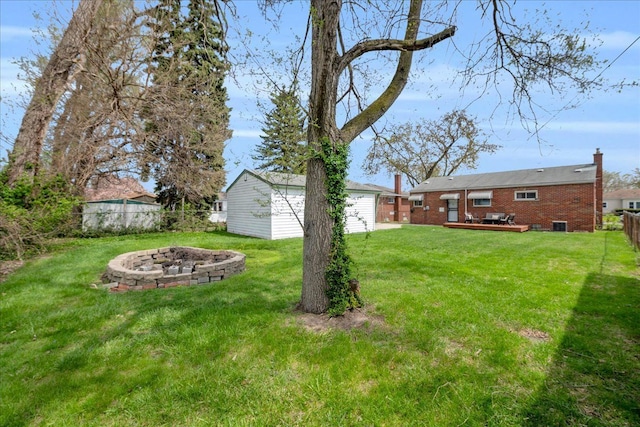 view of yard with an outdoor structure, a wooden deck, a fenced backyard, and an outdoor fire pit