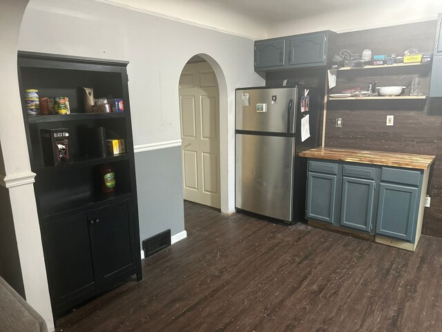 kitchen featuring open shelves, freestanding refrigerator, wooden counters, arched walkways, and dark wood finished floors