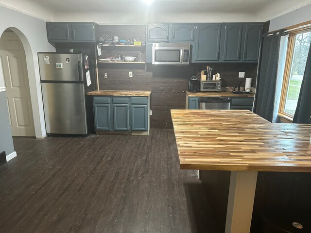 kitchen featuring stainless steel appliances, arched walkways, butcher block countertops, and dark wood-style floors