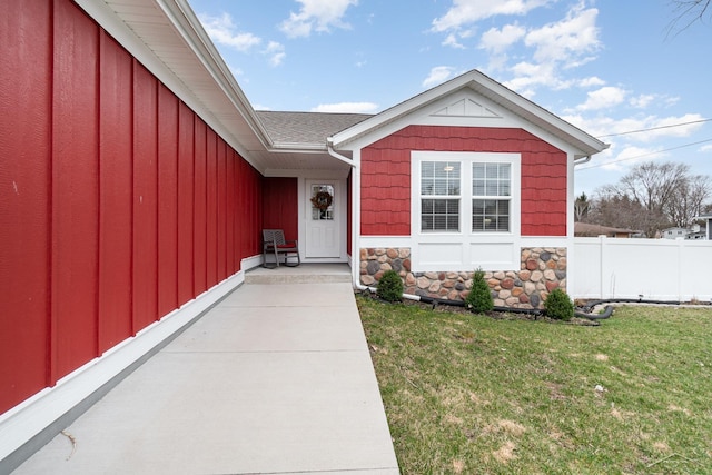 entrance to property with a yard, fence, board and batten siding, and stone siding