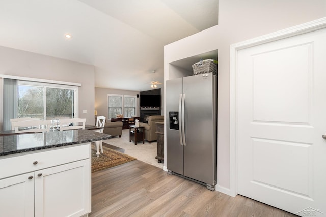 kitchen with stainless steel fridge, dark stone counters, white cabinetry, a ceiling fan, and light wood finished floors