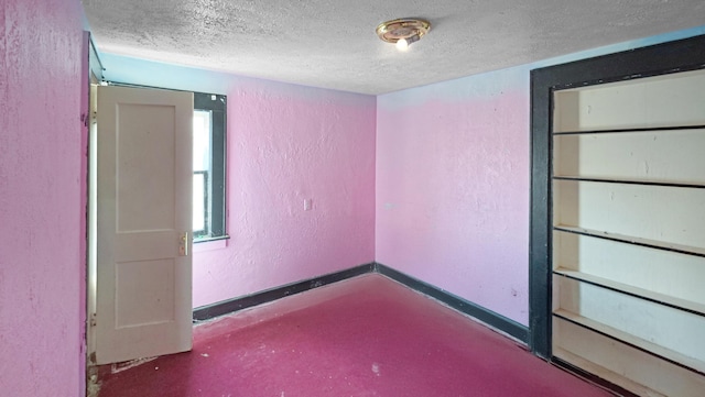 spare room with a textured ceiling, a textured wall, concrete floors, and baseboards