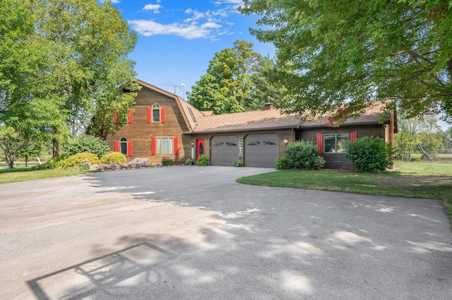 view of front facade with driveway, a chimney, fence, a gambrel roof, and an attached garage