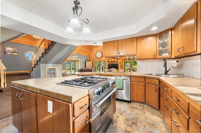 kitchen featuring stone finish flooring, appliances with stainless steel finishes, a sink, light countertops, and glass insert cabinets