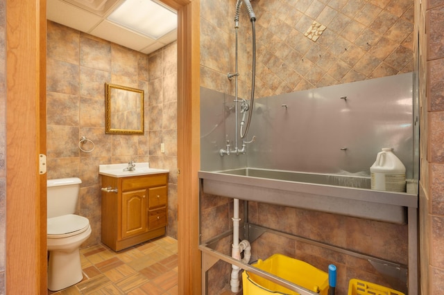 bathroom with vanity, a shower, toilet, and tile walls