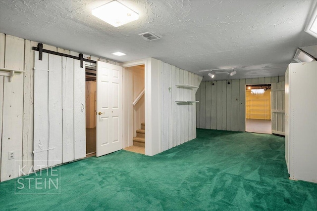 finished basement with carpet floors, visible vents, wooden walls, stairway, and a barn door