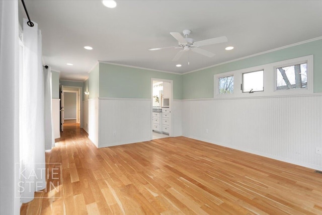 unfurnished room featuring ceiling fan, wainscoting, light wood-style floors, baseboards, and ornamental molding