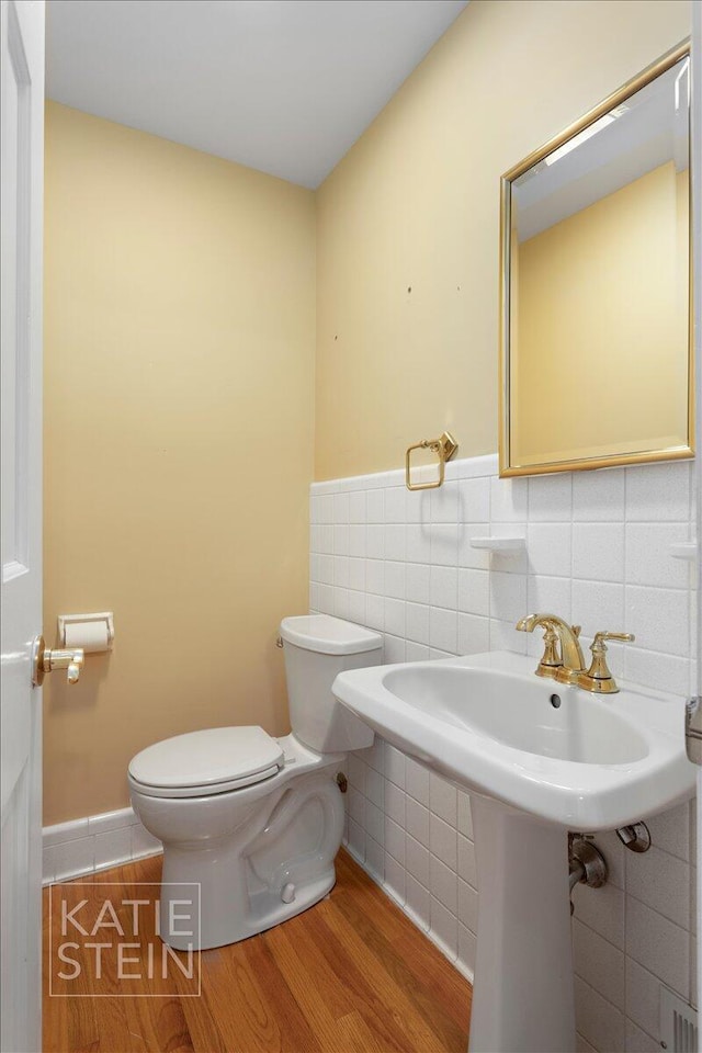 half bathroom with toilet, tile walls, and wood finished floors