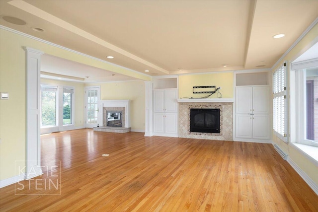 unfurnished living room featuring light wood-type flooring, a tray ceiling, and a tile fireplace