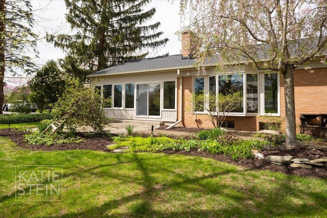 rear view of property featuring brick siding, a yard, and a chimney