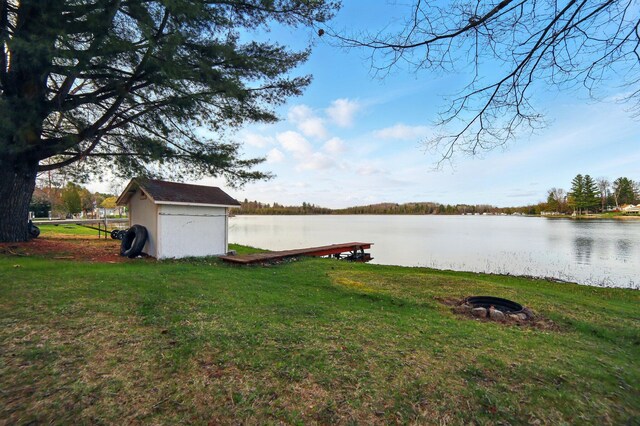 view of yard featuring an outdoor structure, a water view, an outdoor fire pit, and a shed