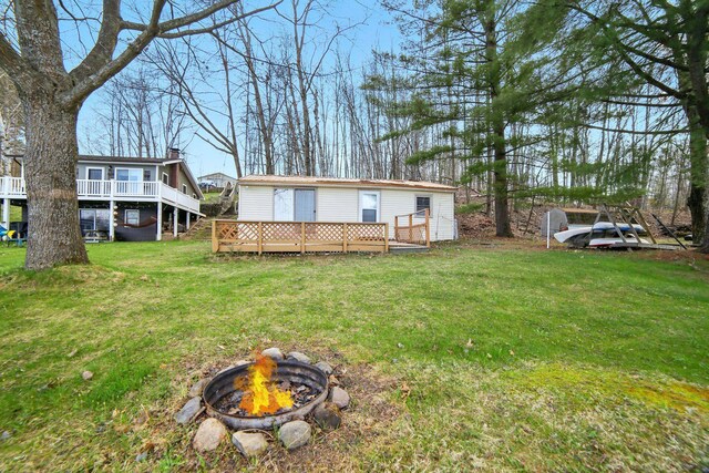 rear view of house featuring a wooden deck, a yard, and a fire pit