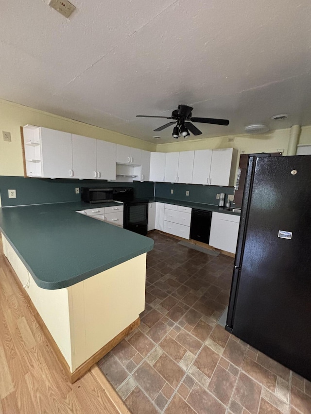 3799 Maple Dr, Wellston, MI 49689 - kitchen with dark countertops, black appliances, a peninsula, and white cabinetry