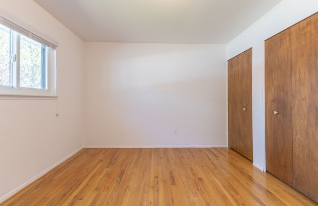 unfurnished bedroom with baseboards, two closets, and light wood finished floors