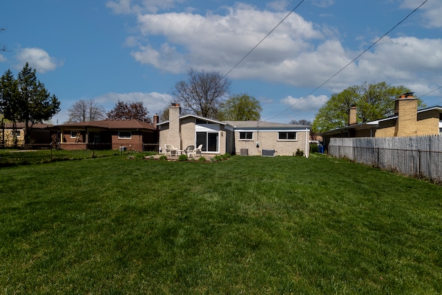back of house featuring a yard, brick siding, fence, and a chimney