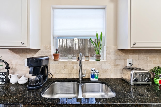 kitchen with a sink, tasteful backsplash, dark stone countertops, and white cabinetry