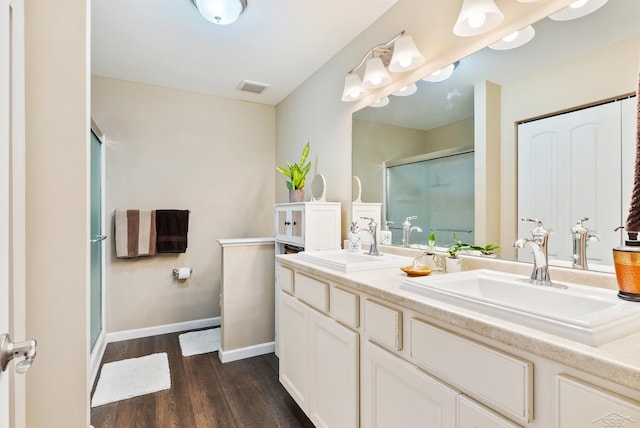 bathroom featuring double vanity, a shower stall, a sink, and wood finished floors