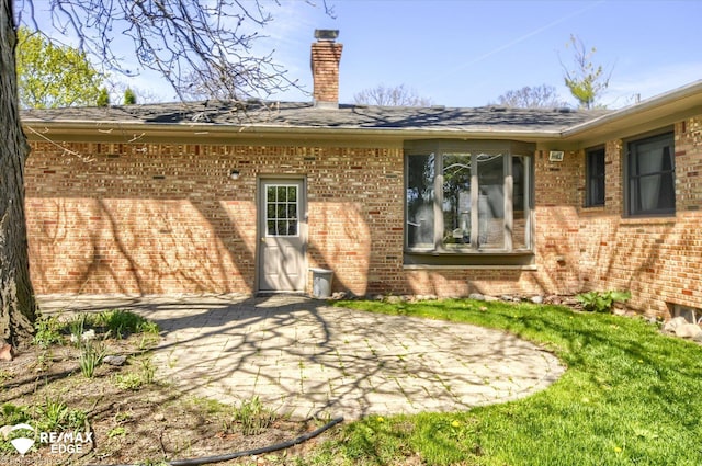 back of property featuring brick siding, a chimney, and a patio area