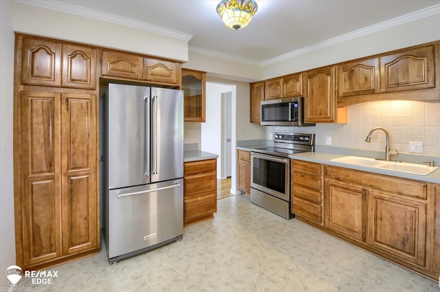 kitchen featuring brown cabinetry, ornamental molding, light countertops, a sink, and appliances with stainless steel finishes