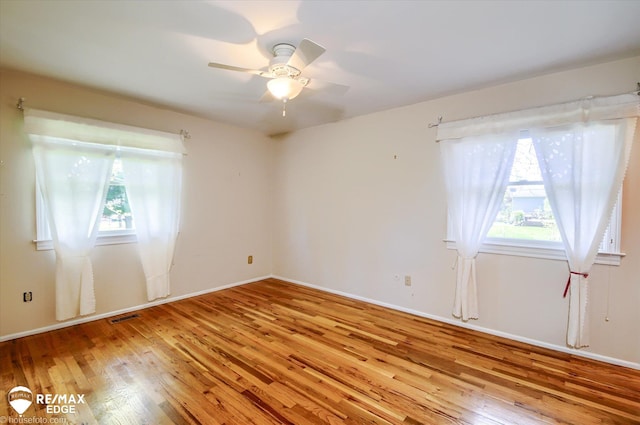 spare room featuring wood-type flooring, ceiling fan, visible vents, and a wealth of natural light