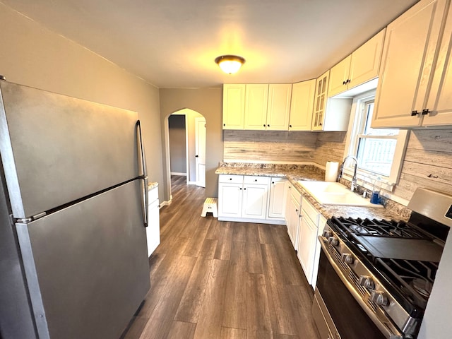 kitchen featuring decorative backsplash, dark wood-style flooring, arched walkways, a sink, and stainless steel appliances