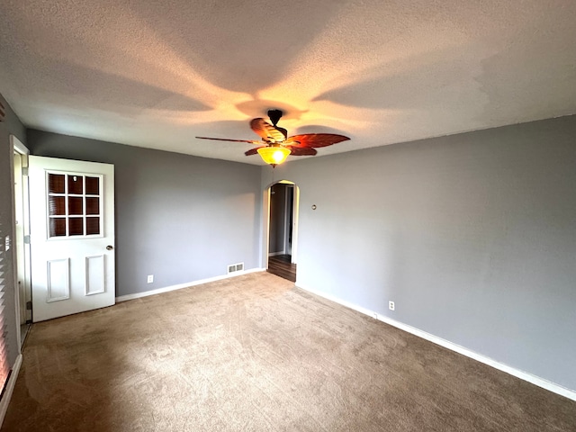 carpeted empty room with arched walkways, ceiling fan, a textured ceiling, and visible vents